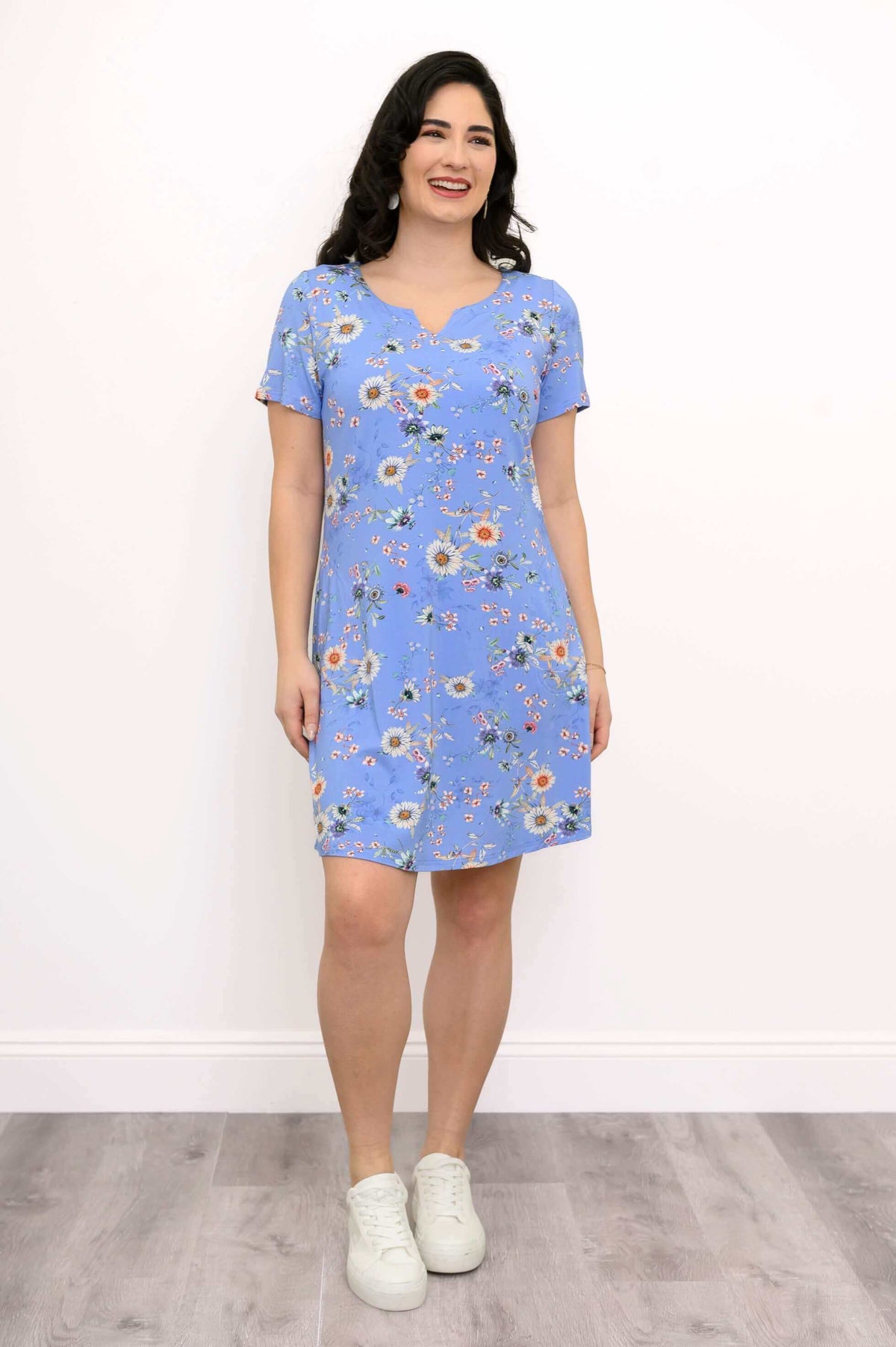 Model smiling in blue floral knee-length dress with short sleeves and white sneakers