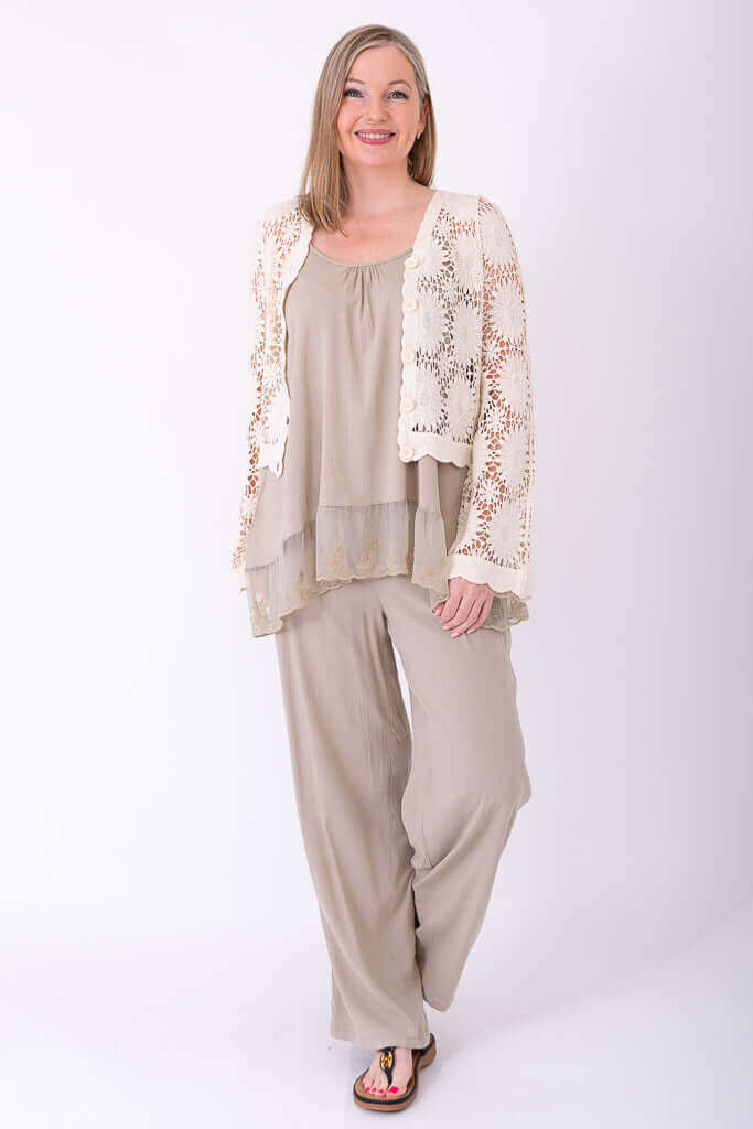 Woman standing and smiling, wearing crochet cardigan over a layered beige ensemble