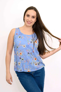 Woman posing in blue floral tank top and jeans, holding her hair with a smile