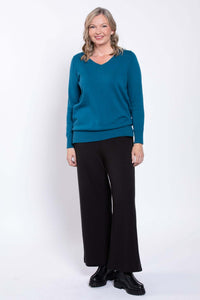 Woman smiling in black wide-leg pants and teal sweater, full front view
