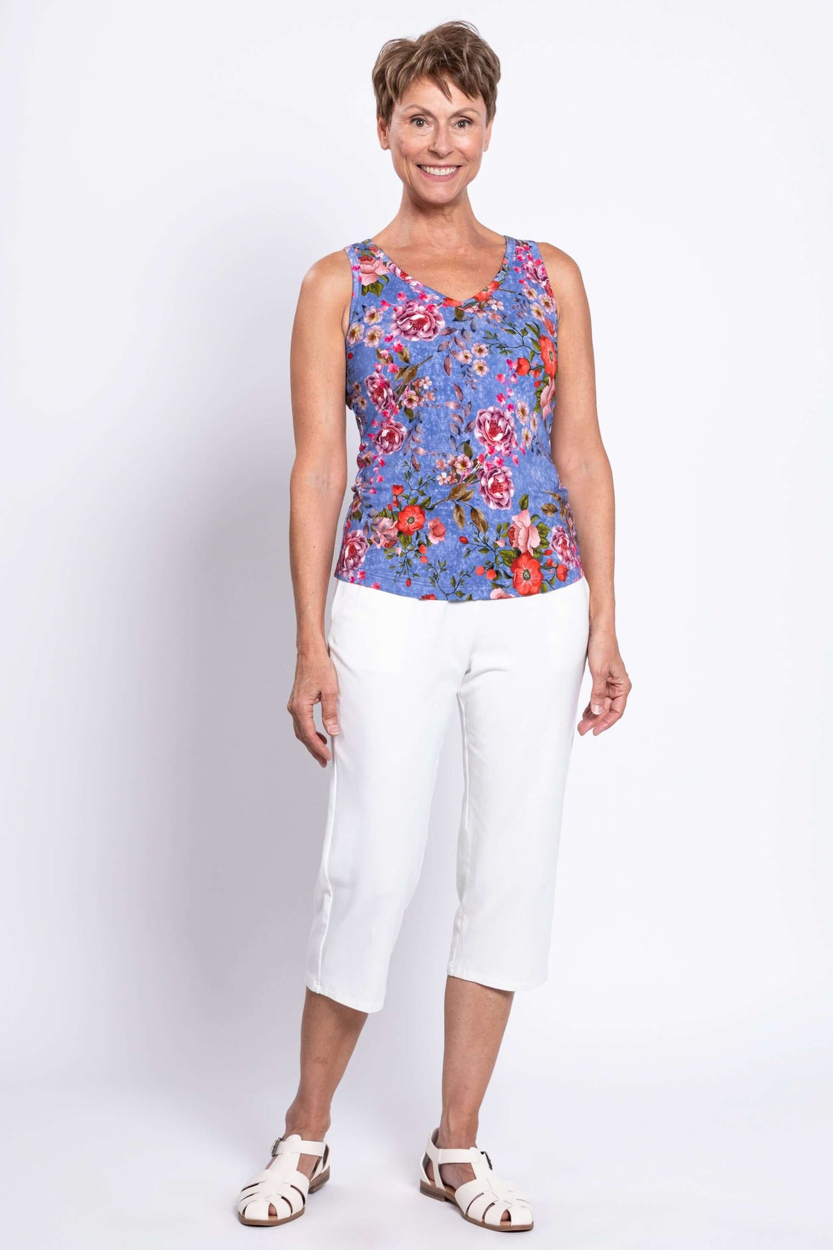 Full body front view of woman smiling in blue floral bamboo tank and white pants