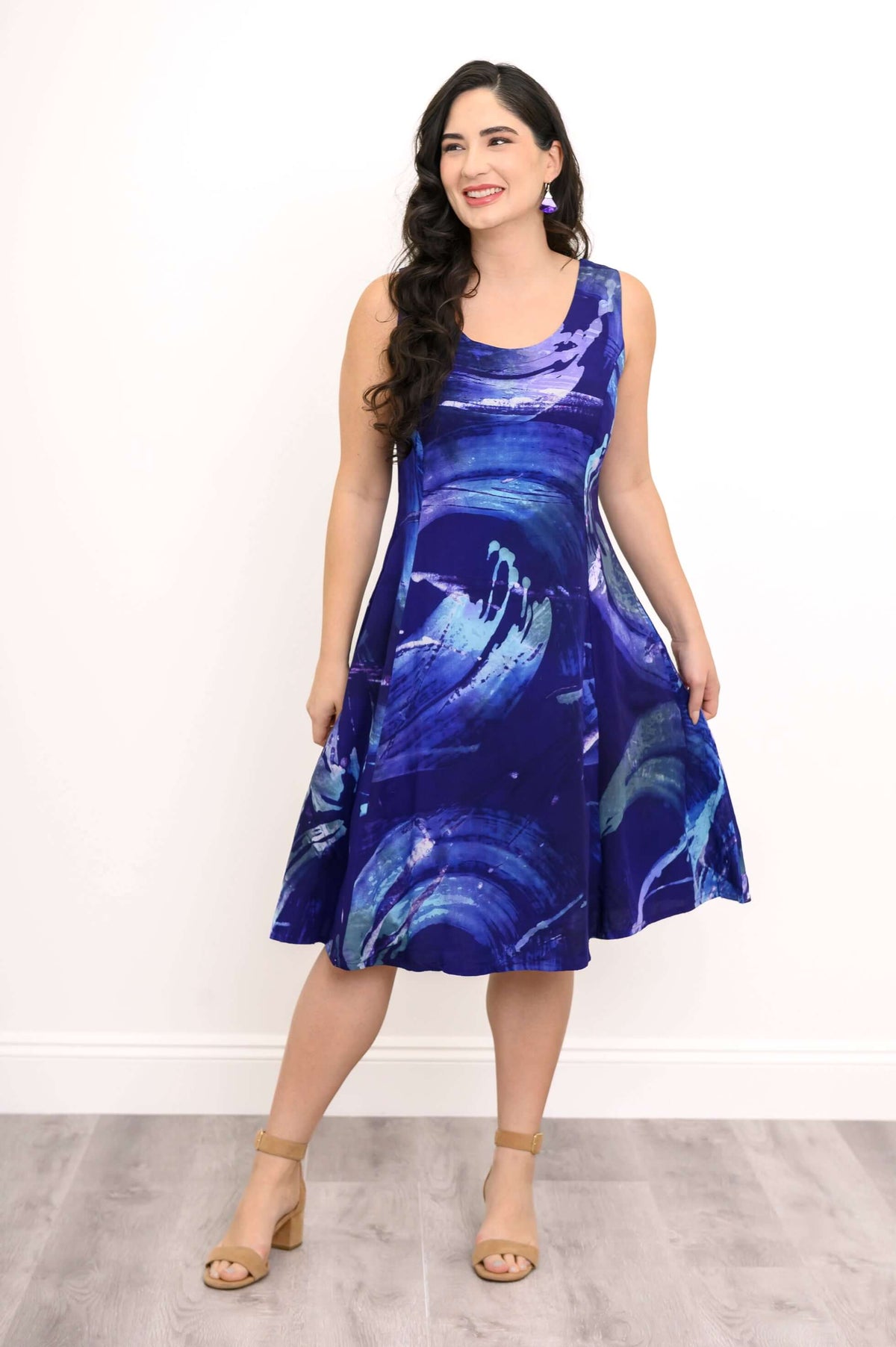 Smiling woman in a blue swirl print sleeveless dress, standing against a white wall