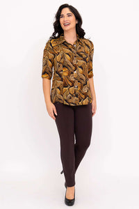 Woman smiling, wearing autumn leaf print blouse with brown pants and black heels
