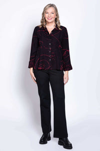 Woman smiling, wearing black button-front blouse with long sleeves and abstract red print