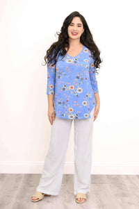 Woman smiling in a blue floral V-neck bamboo top with white pants
