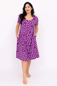 Smiling woman in purple dot nightdress with hands in pockets