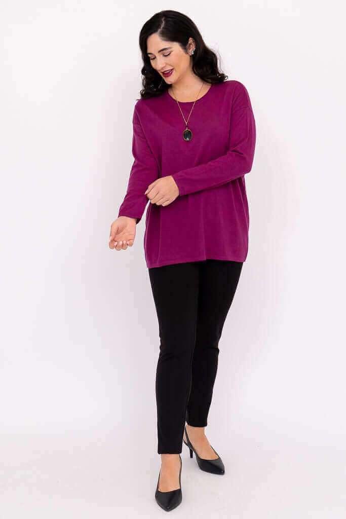 Woman smiling and looking down in a vivid pullover sweater and black pants