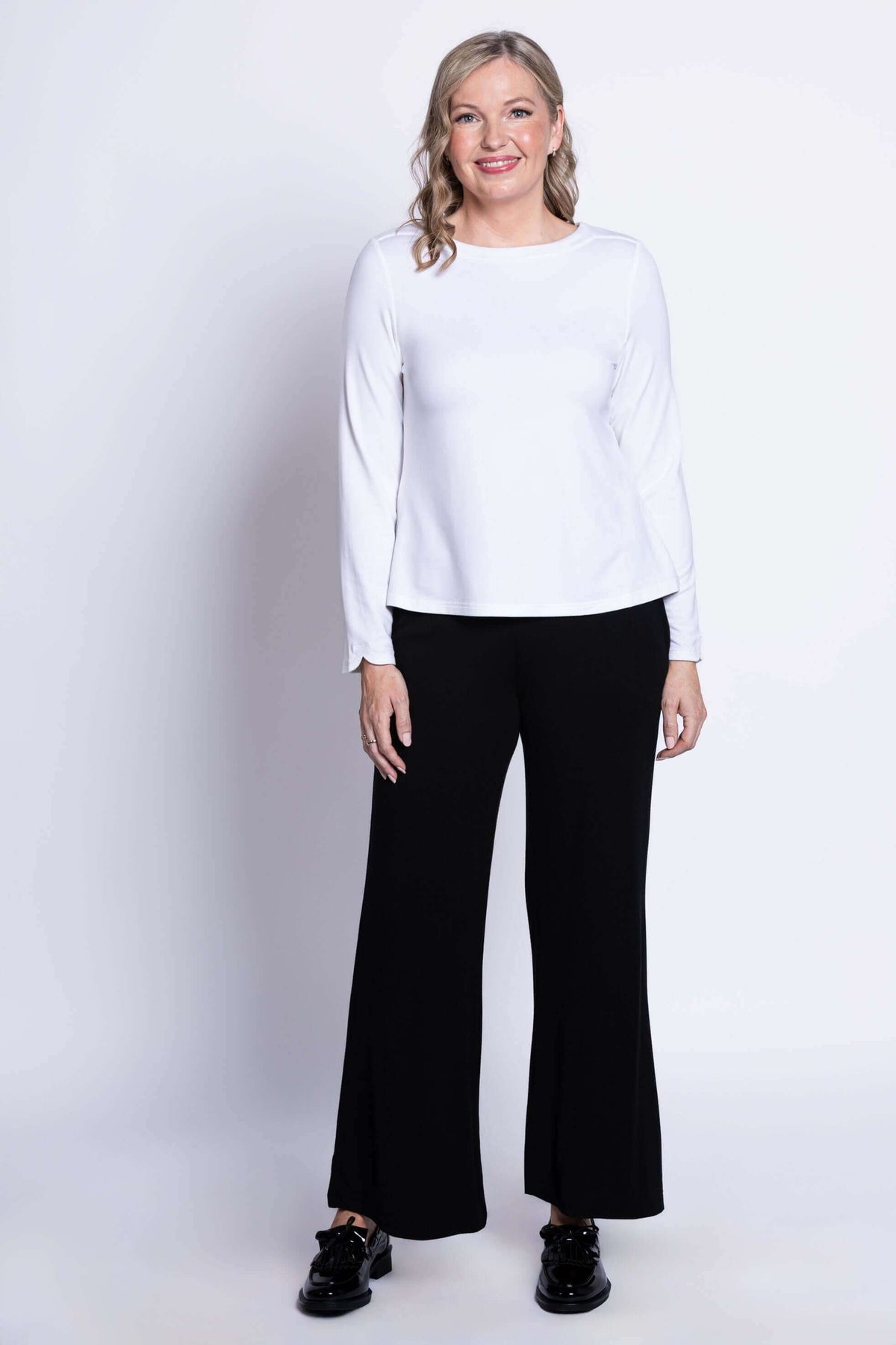 Smiling woman wearing white boat neck top and black pants, full body view