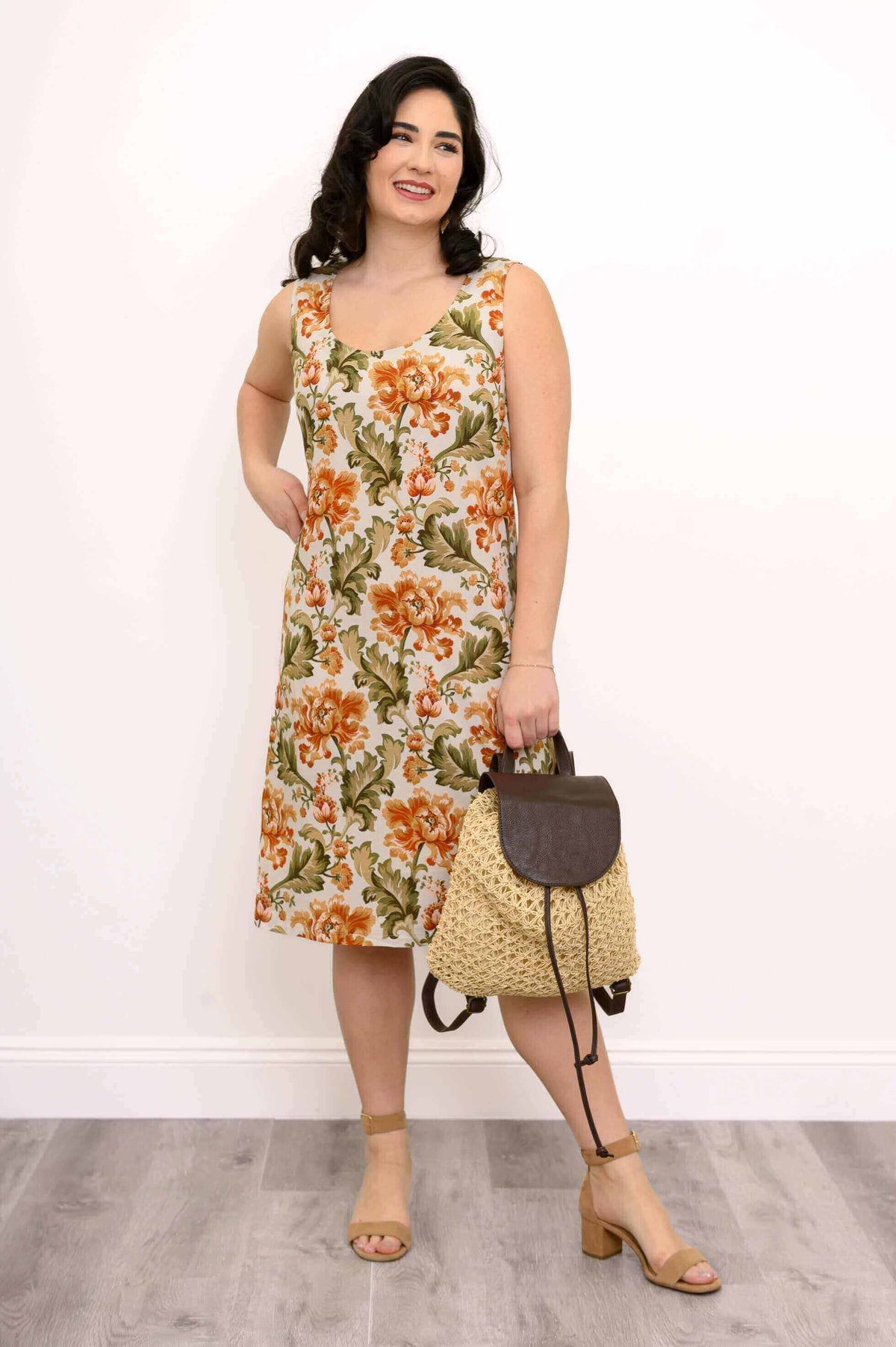 Smiling woman modeling a sleeveless floral A-line dress with a straw bag