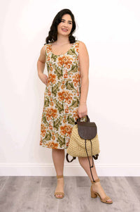 Smiling woman modeling a sleeveless floral A-line dress with a straw bag