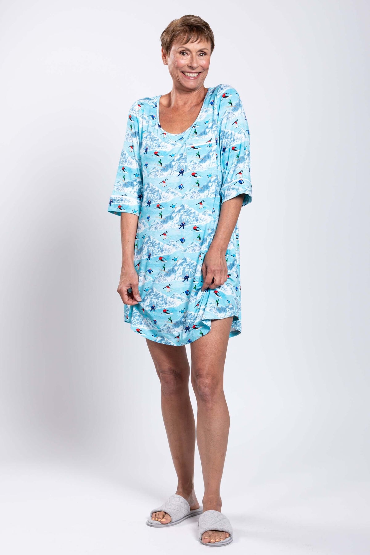 Woman smiling and posing in a blue skier-pattern sleepshirt with slippers