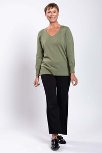 Woman smiling, wearing a green V-neck sweater and black pants, full-body front view