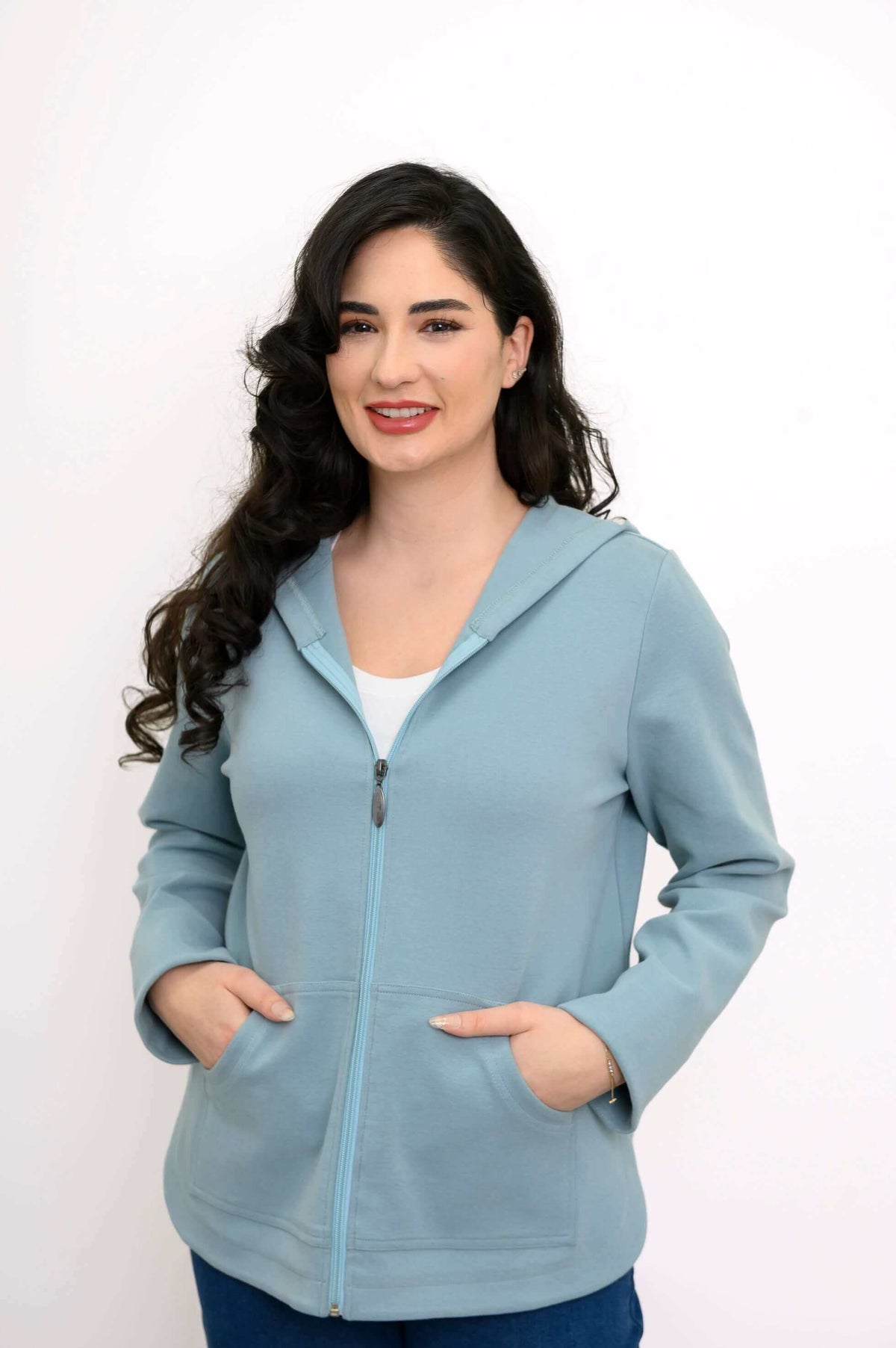 Woman smiling in a light blue zip hoodie with hands in pockets, front view