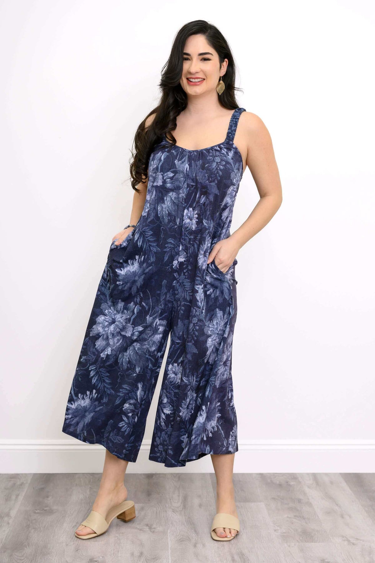 Woman smiling in a navy floral jumpsuit with wide legs and posing with her hands in her pockets