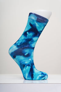 Vibrant blue and dark navy swirl crew sock displayed on a white mannequin foot against a light gray studio backdrop.