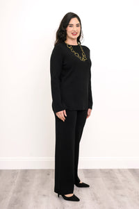 Profile shot of a women's dark charcoal sweater with long bell sleeves, styled with matching knit trousers.