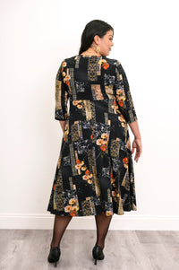 Back view of a woman wearing a black and orange floral midi dress showing the clean drape across the shoulders.