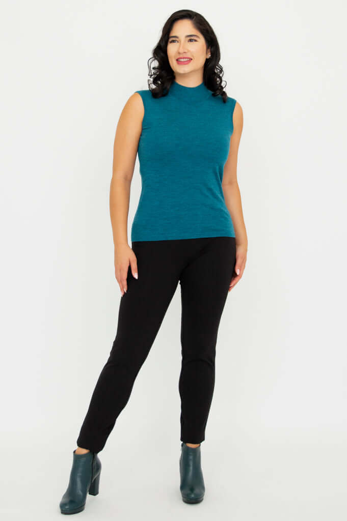 Woman standing in teal sleeveless merino wool sweater and black pants, looking left