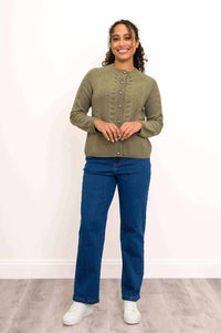Woman standing in green cable knit cardigan with hands together, blue jeans, white sneakers