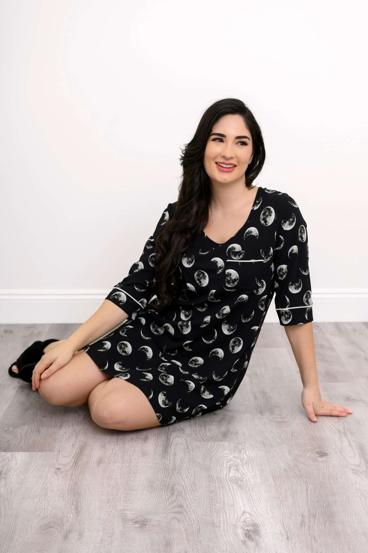 Woman sitting on the floor wearing a black moon phase pattern sleepshirt
