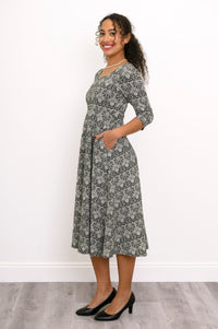 Angled front view of a woman modeling a dark grey floral midi dress showing the flowy drape