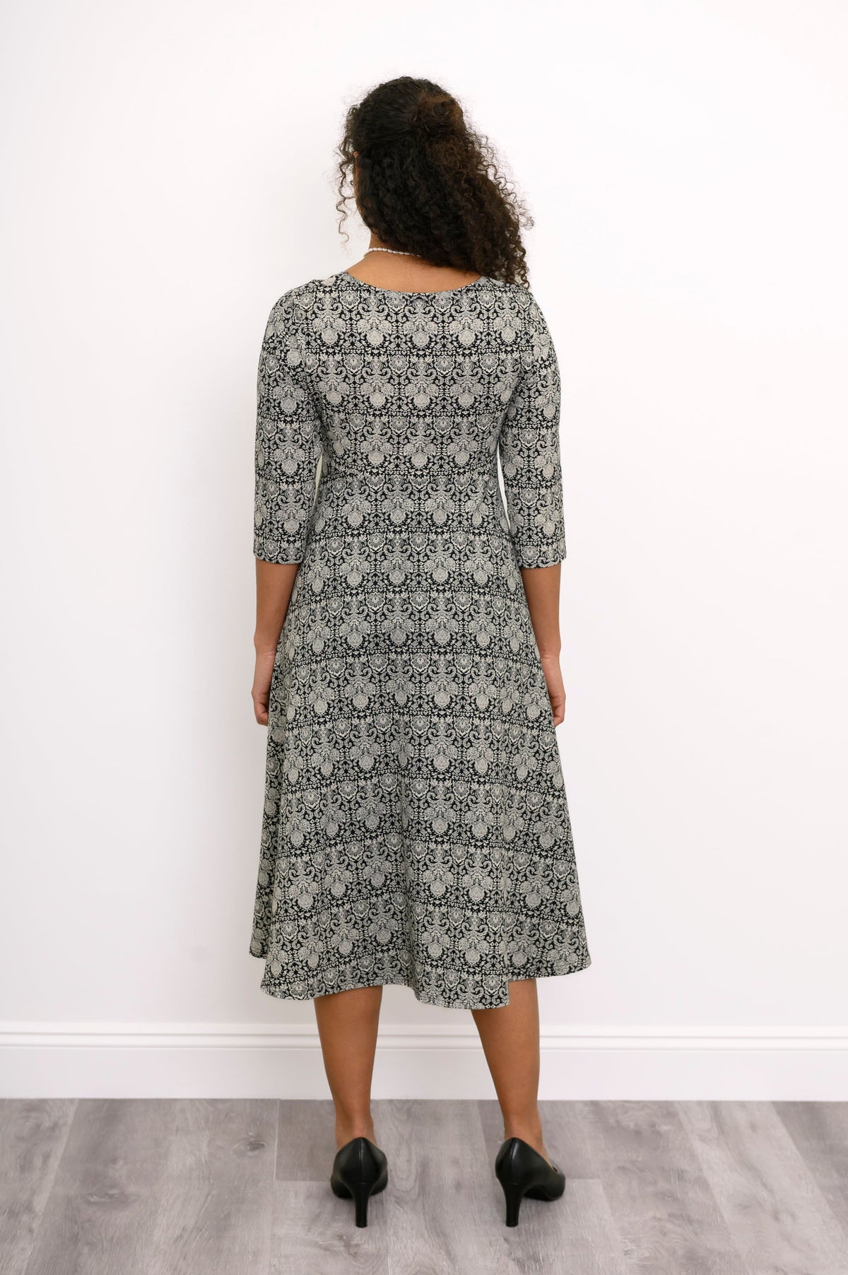 Back view of a woman wearing a grey patterned midi dress with a clean, seamless finish across the shoulders.