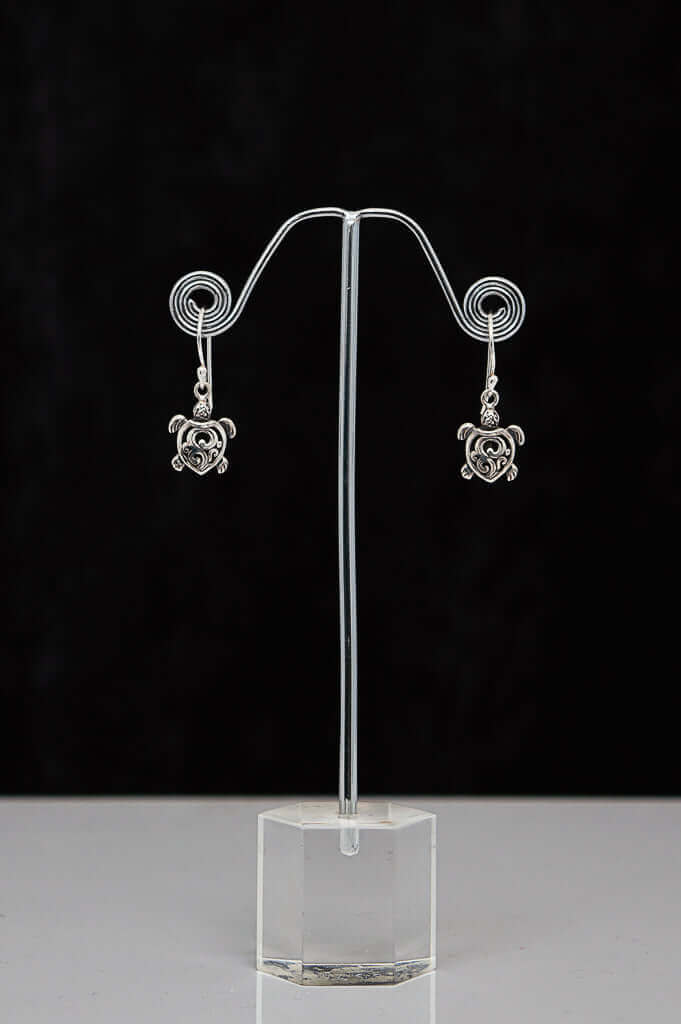 Pair of sterling silver turtle heart earrings displayed on a metal stand with black background