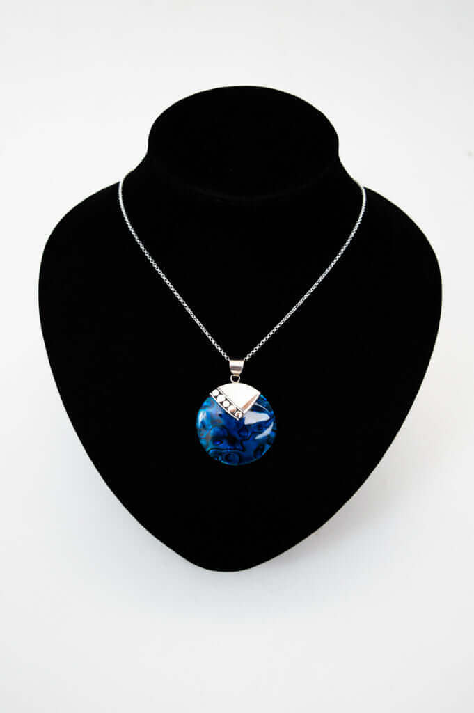 Sterling silver necklace with blue round pendant displayed on black necklace stand