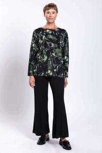 Straight-on full-length view of woman in forest print long-sleeve top and black trousers