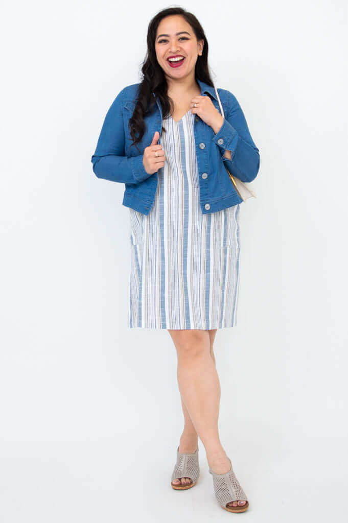 Woman smiling in a striped dress styled with a denim jacket and open-toe sandals
