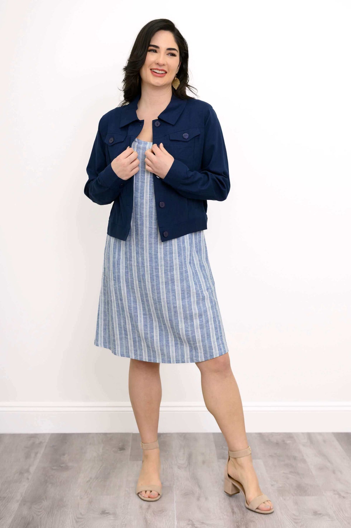 Woman wearing blue striped shift dress styled with a navy jacket, smiling.