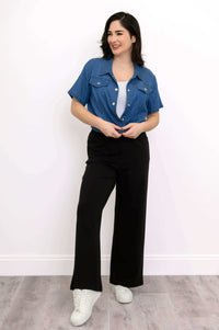 Woman in open blue cropped denim jacket, white tank top, and black pants