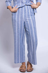 Front view of woman lifting up her top to show the elastic waistband of her linen blend striped pants
