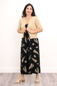 Woman styling beige cardigan over a black printed dress, holding the cardigan front