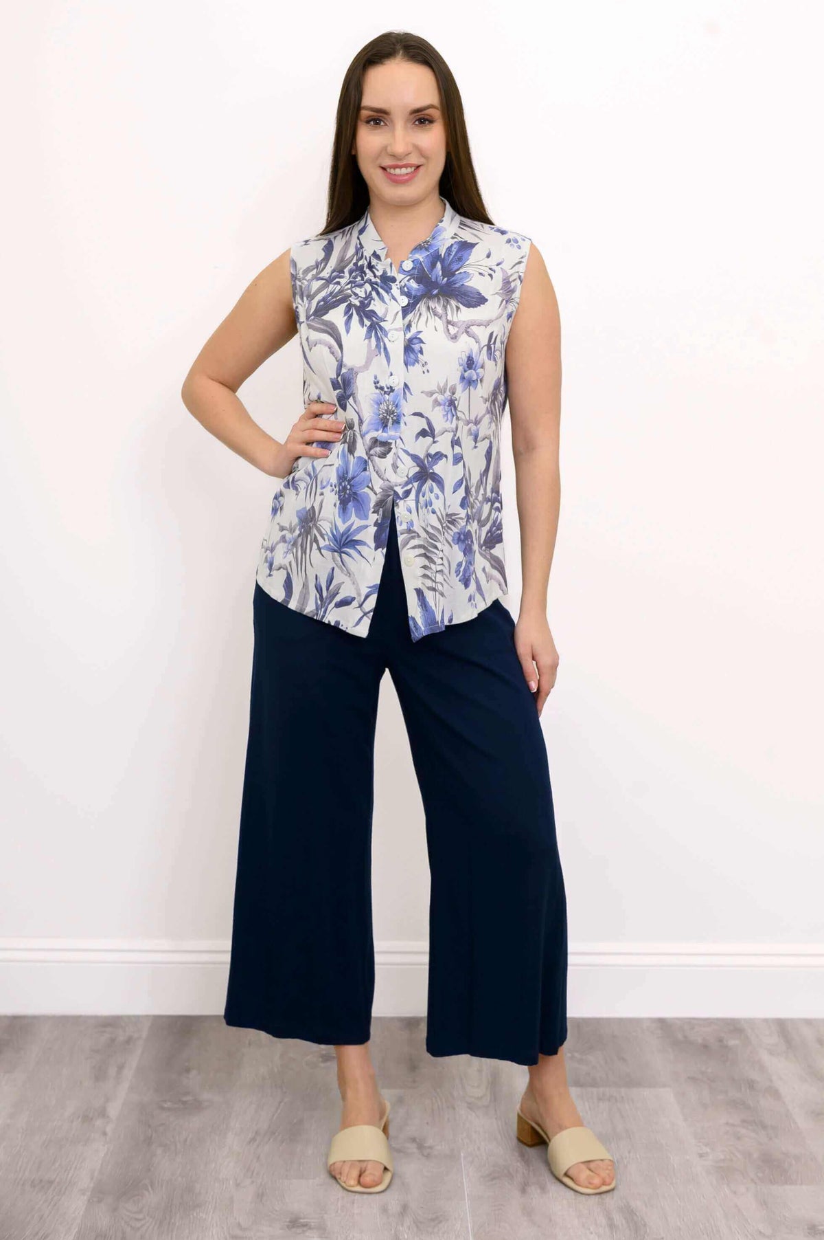 Woman with hand on hip showcasing blue floral sleeveless blouse and navy pants