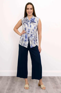 Woman with hand on hip showcasing blue floral sleeveless blouse and navy pants