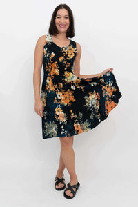 Woman posing in a black, orange, and yellow floral print A-line dress, holding skirt