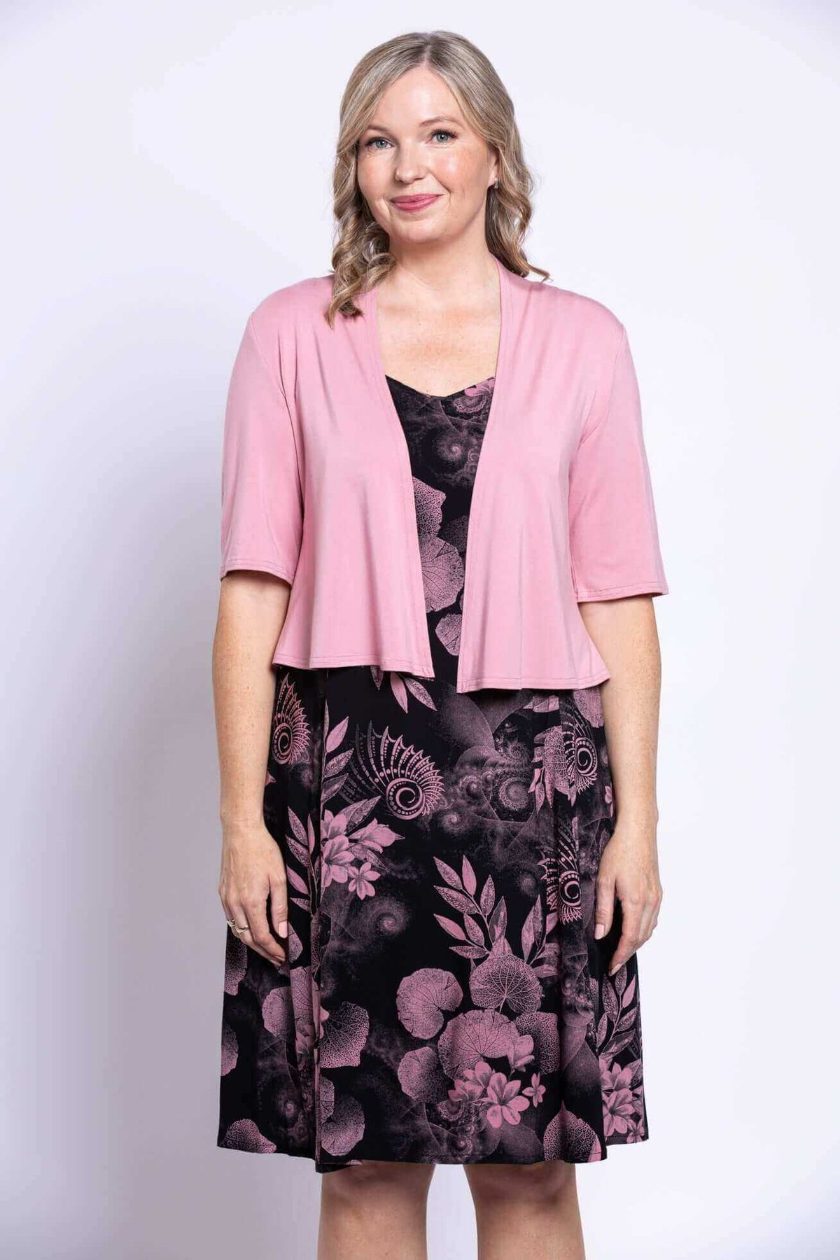 Woman wearing a black dress with pink floral print and a light pink cardigan