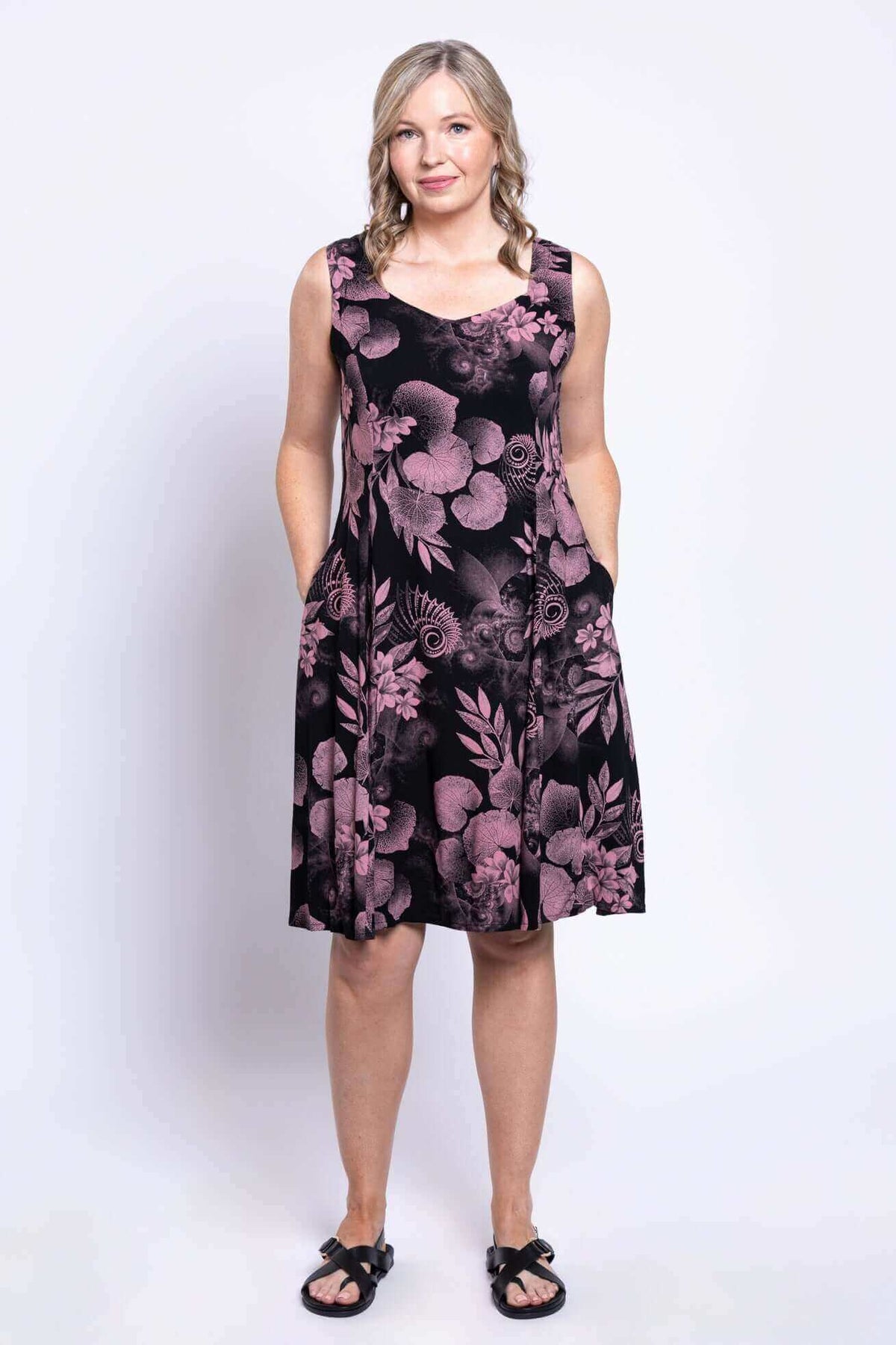 Woman in pink floral sleeveless dress with hands in pockets, standing front-facing