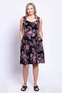 Woman in pink floral sleeveless dress with hands in pockets, standing front-facing