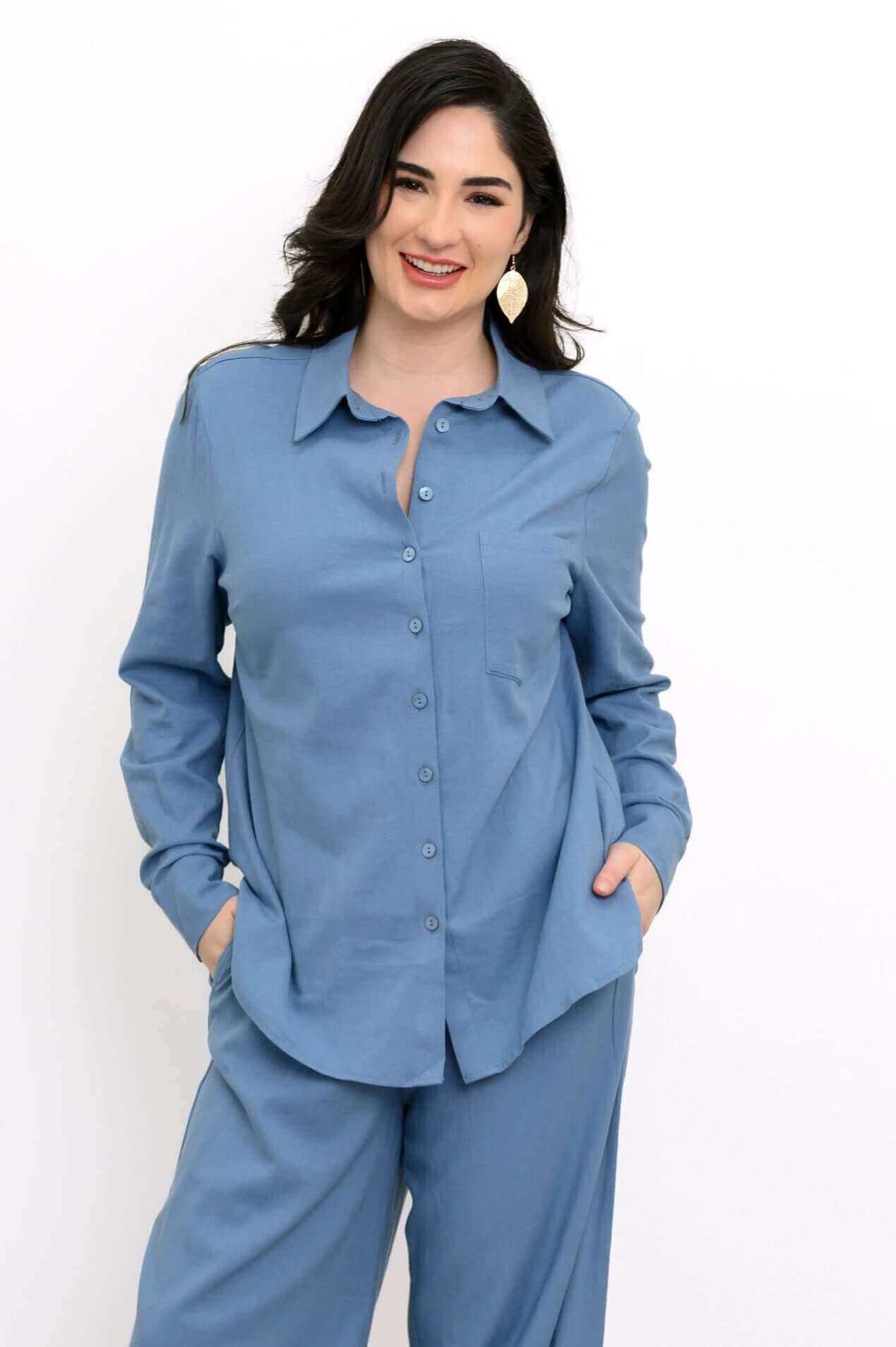 Woman wearing a tailored blue button-up shirt and matching relaxed pants, hands in pockets