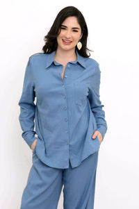 Woman wearing a tailored blue button-up shirt and matching relaxed pants, hands in pockets