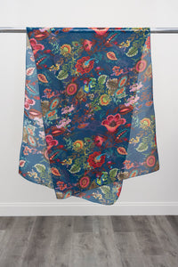 A large teal silk scarf with a multicolour paisley pattern displayed on a metal rod against a white background, front view