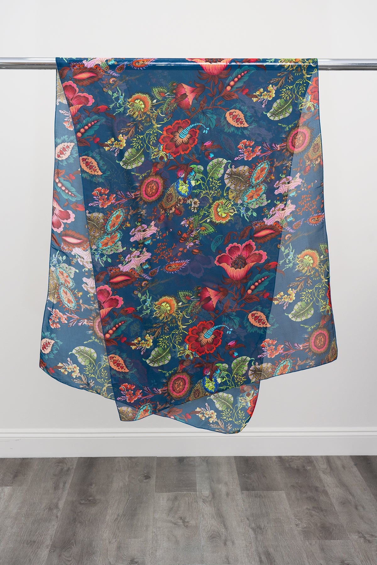 A large teal silk scarf with a multicolour paisley pattern displayed on a metal rod against a white background, front view