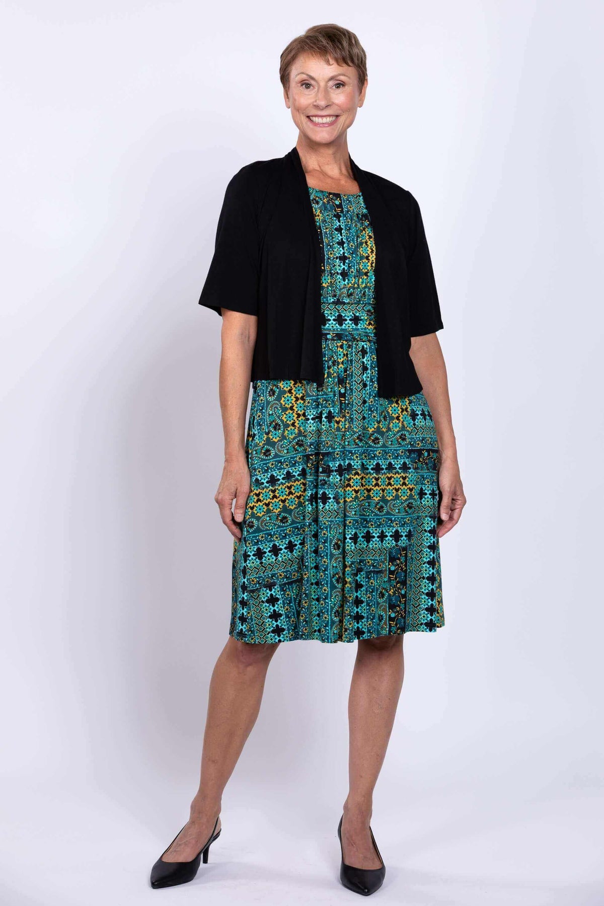 Woman wearing teal and yellow sleeveless dress and black cardigan, posing