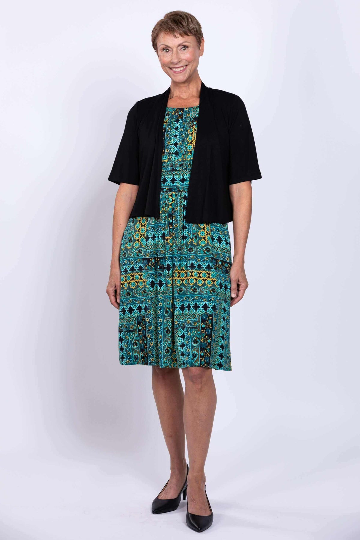 Woman in a teal and yellow patterned dress with a black short-sleeved cardigan
