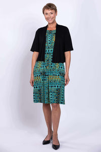 Woman in a teal and yellow patterned dress with a black short-sleeved cardigan