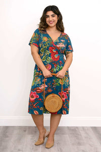 Woman in teal floral bamboo dress holding a round wicker bag, smiling