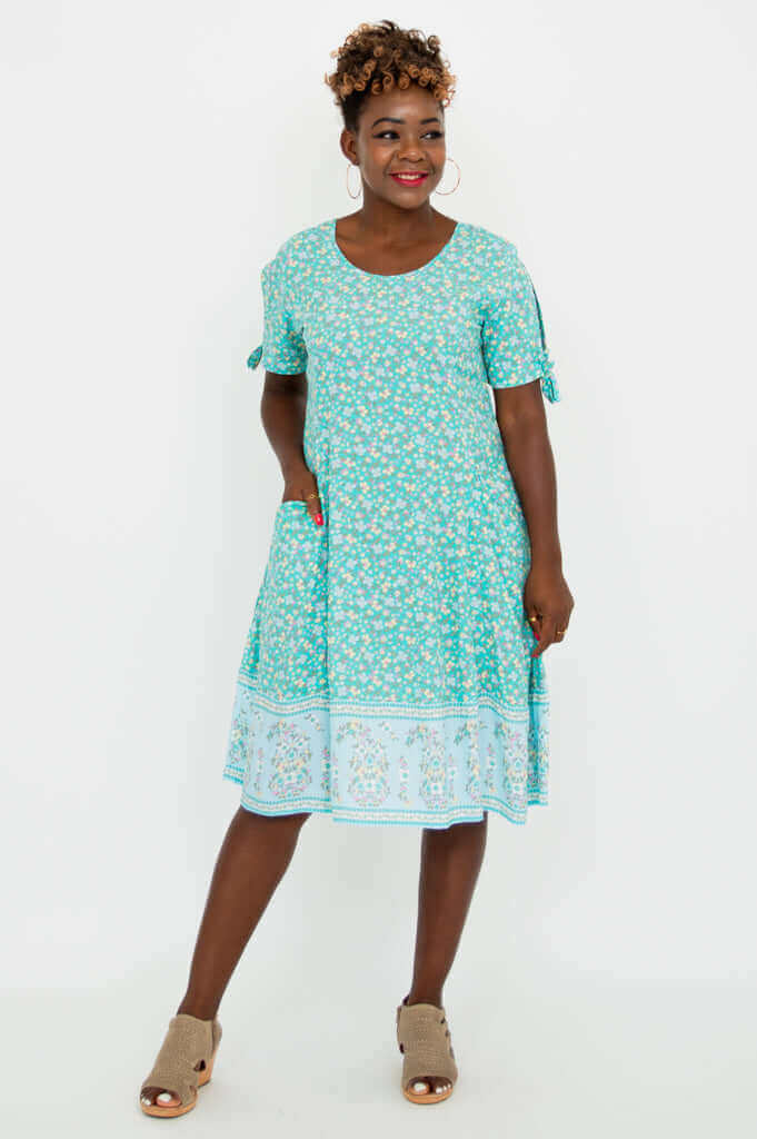 Woman wearing a teal floral midi dress with tie sleeve accents and pockets