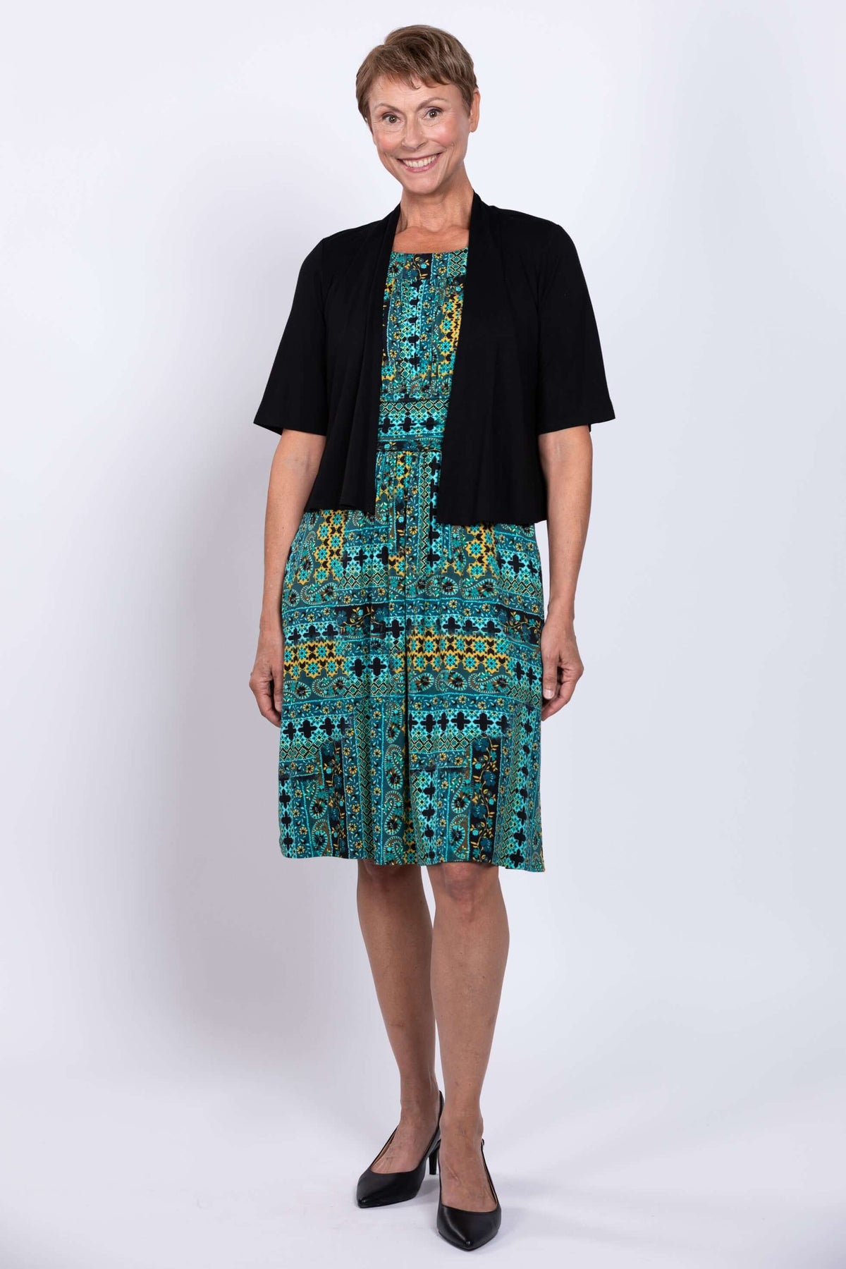 Woman in teal patterned dress layered with black short sleeve cardigan